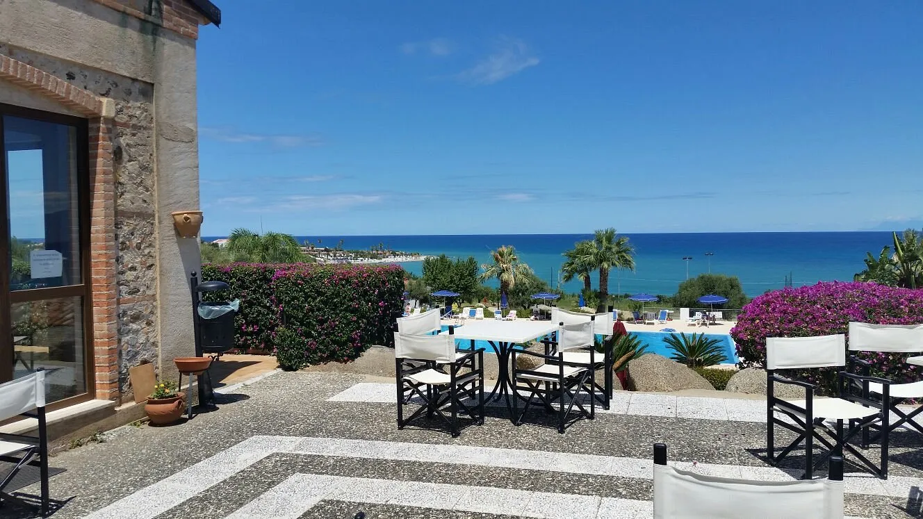 Terrazza con tavoli e sedie e vista panoramica sul mare e sulla piscina