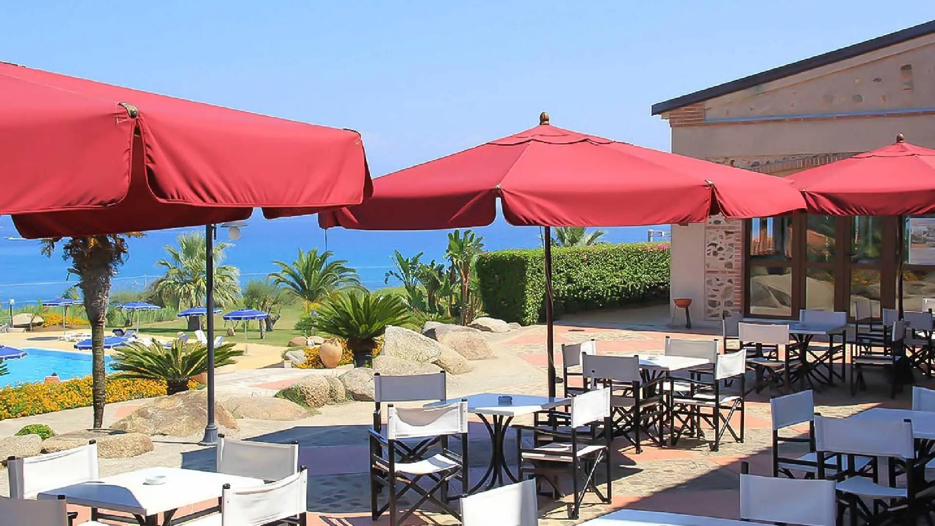 Terrazza ristorante con ombrelloni rossi e tavoli affacciata su piscina e mare