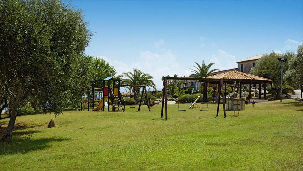 Area giochi per bambini con altalene e scivolo nel prato verde