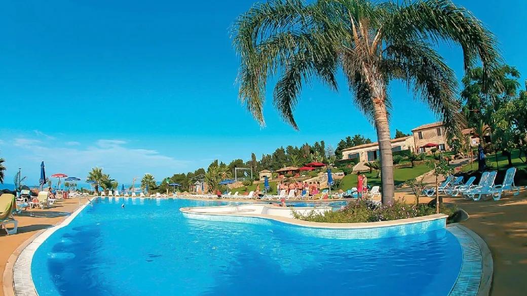 Piscina con palma e lettini circondata da vegetazione e casale