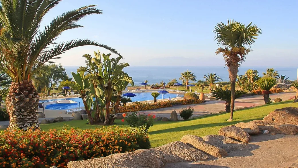 Giardino con palme e fiori al tramonto con piscina e mare sullo sfondo