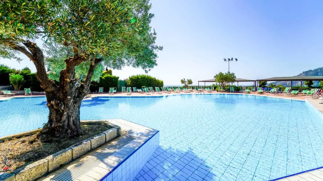 Ampia piscina con ulivo centrale, lettini verdi e vista mare