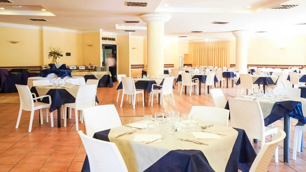 Sala ristorante interna con tavoli apparecchiati e tovaglie blu e beige