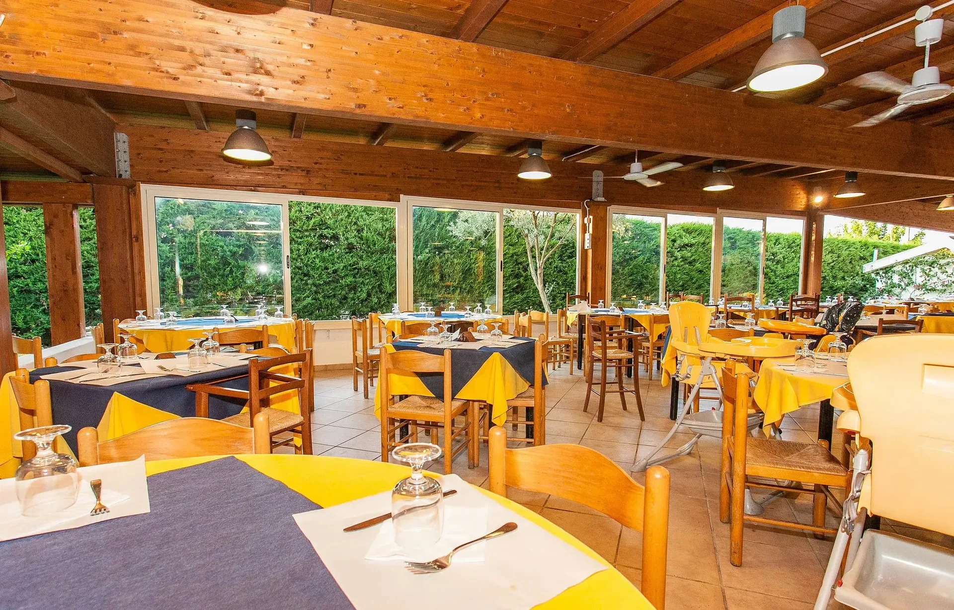 Sala ristorante con soffitto in legno, tavoli apparecchiati e vista sul verde