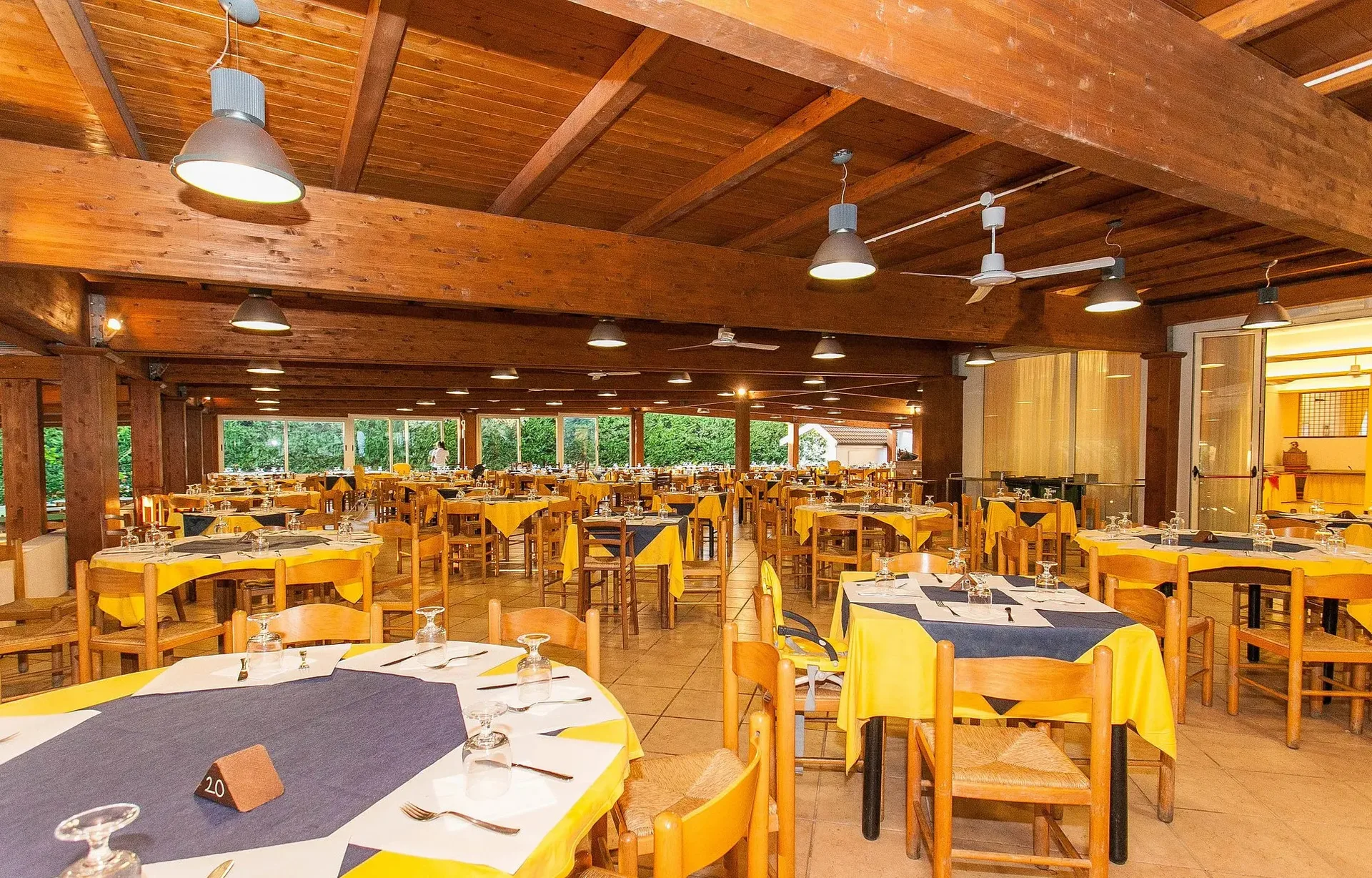 Ampia sala ristorante con tovaglie gialle e blu e travi in legno a vista