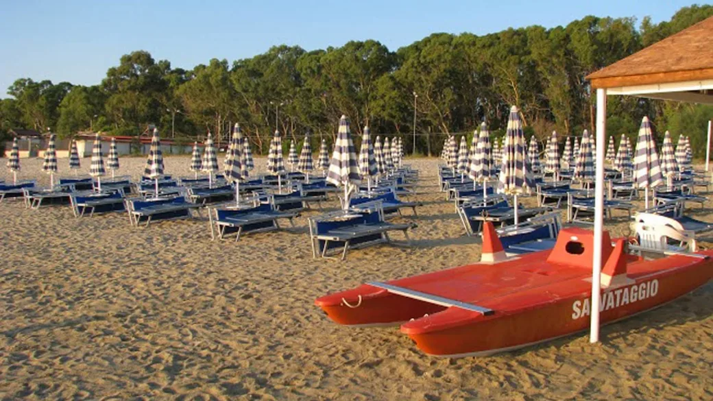 Spiaggia al tramonto con ombrelloni chiusi, lettini blu e pattino di salvataggio