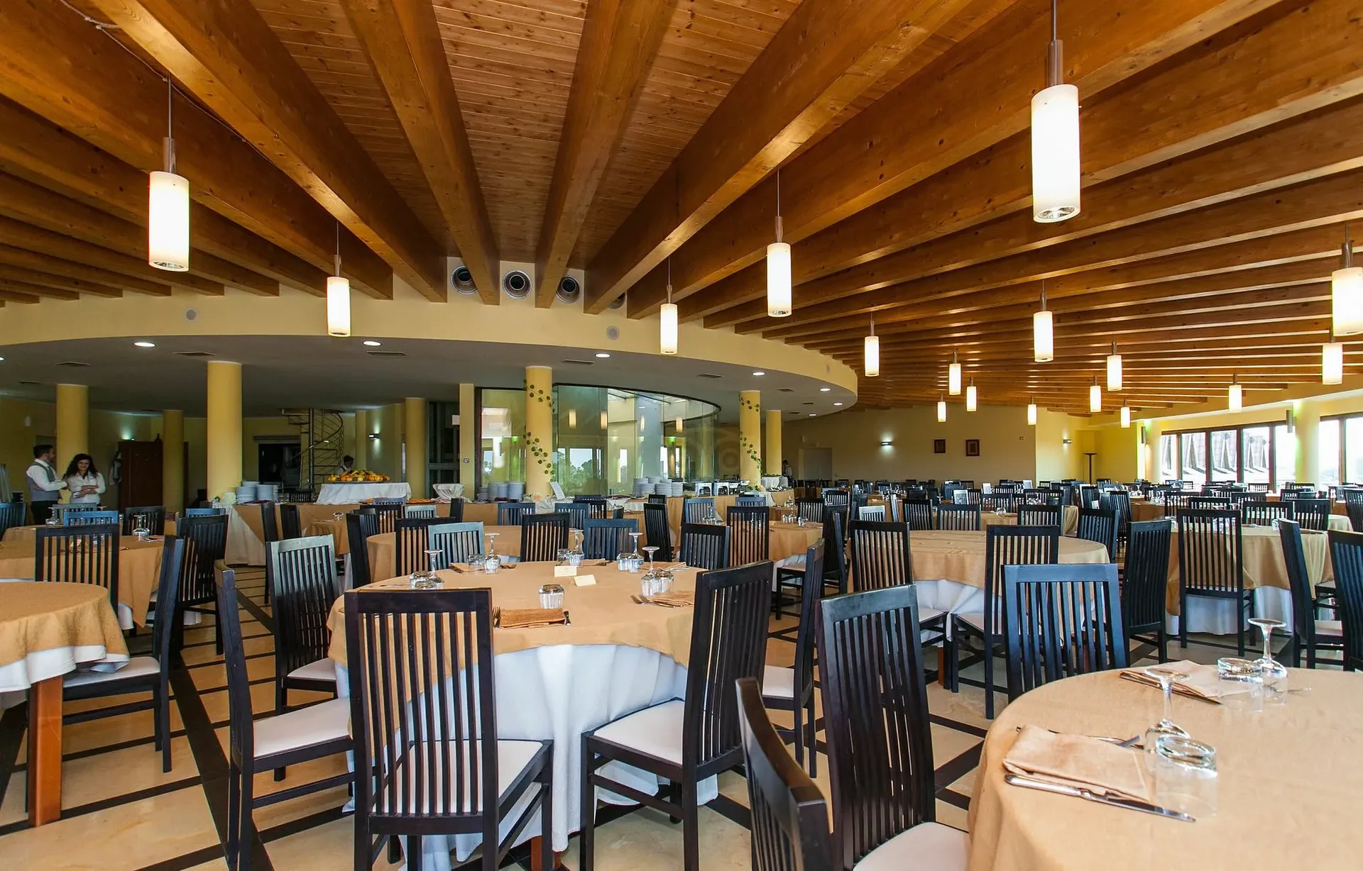 Sala ristorante interna con soffitto in travi di legno, tavoli rotondi e sedie scure