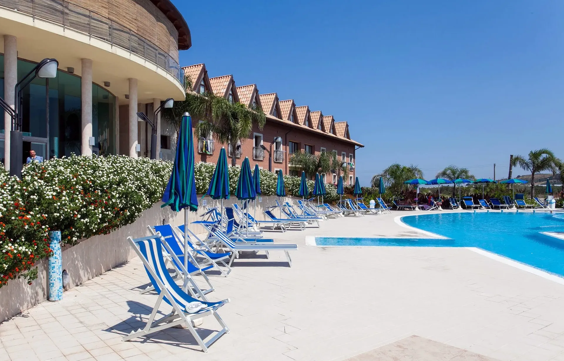 Bordo piscina con lettini e sdraio blu accanto all'edificio circolare del resort
