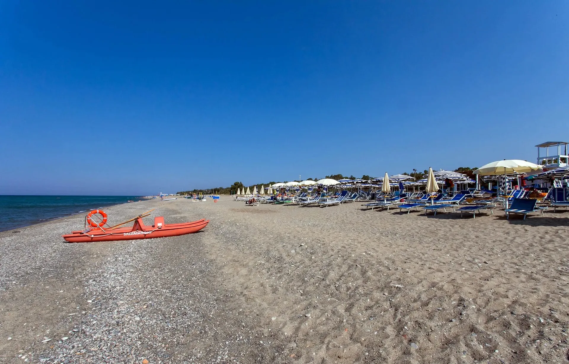 Spiaggia sabbiosa con lettini, ombrelloni e pattino di salvataggio arancione