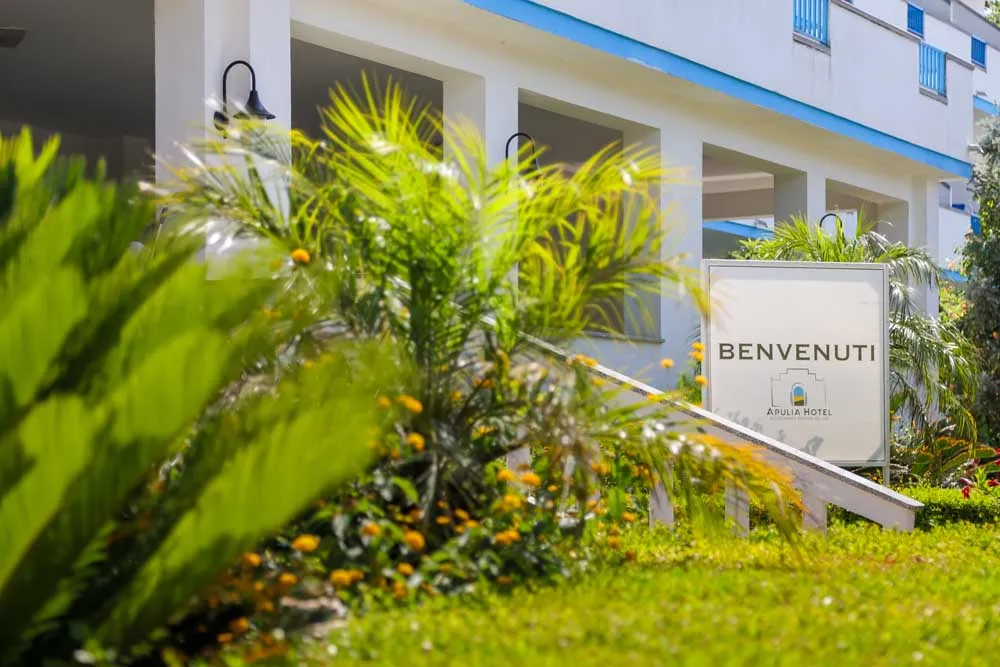 Cartello di benvenuto dell'Apulia Hotel tra la vegetazione all'ingresso