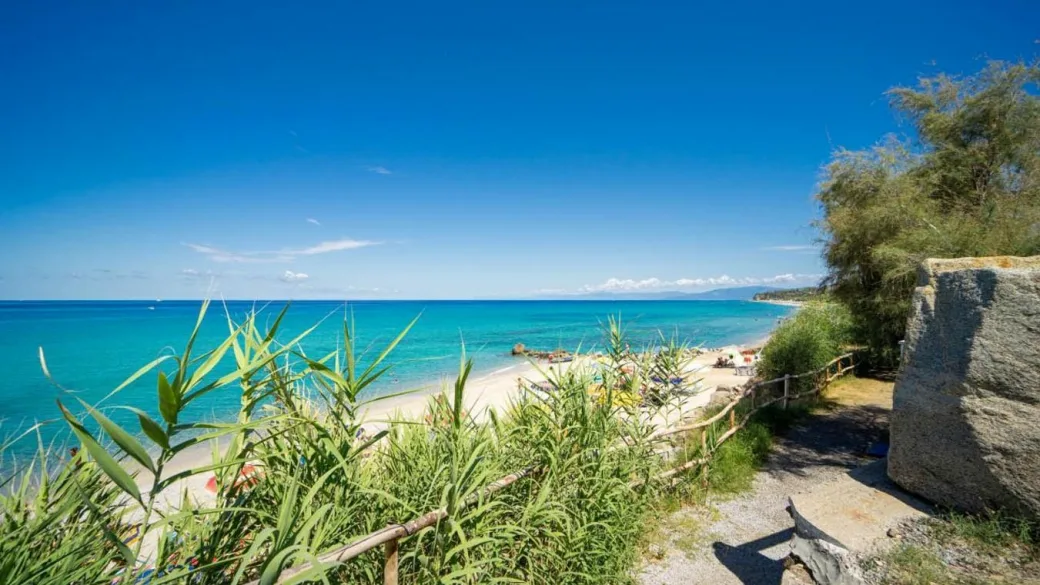 Spiaggia sabbiosa vista dalla vegetazione con mare azzurro cristallino