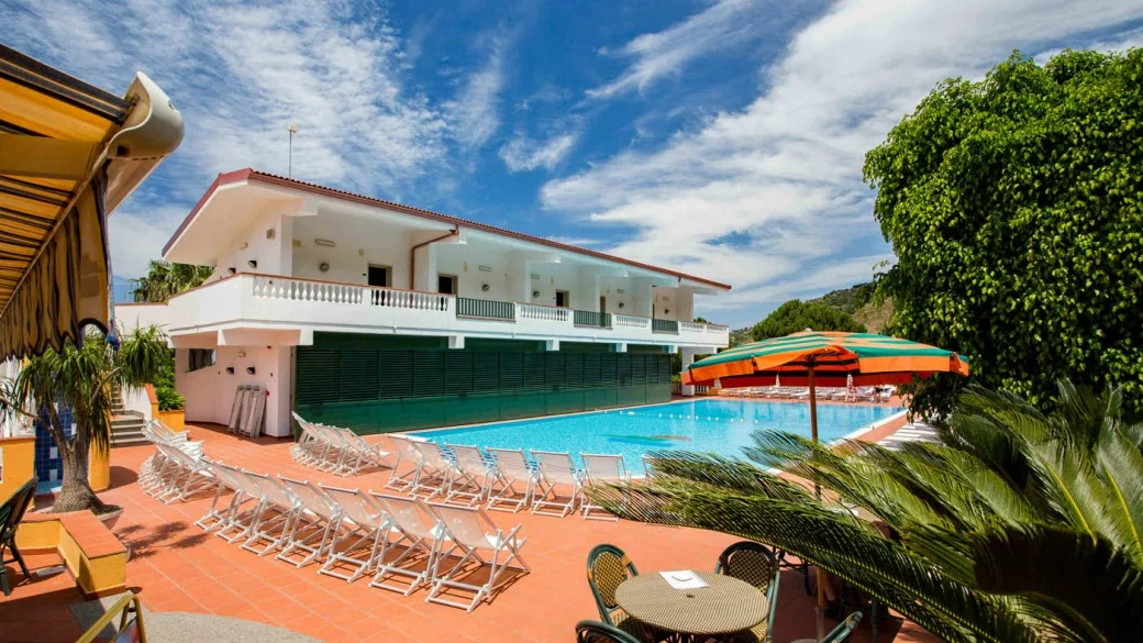 Piscina con lettini bianchi e ombrelloni colorati vicino all'edificio
