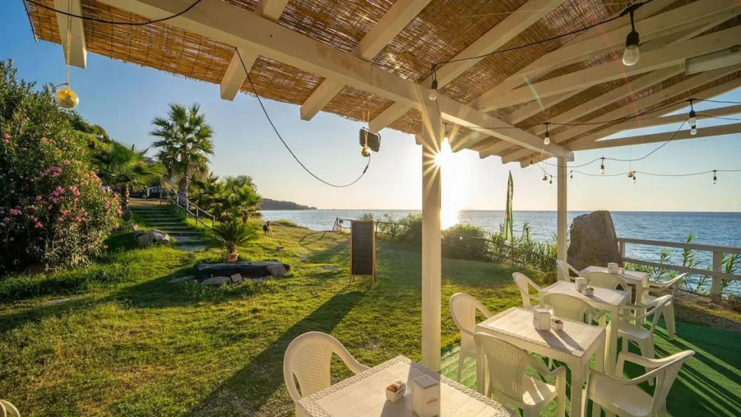 Area ristoro all'aperto con pergolato e vista sul mare al tramonto