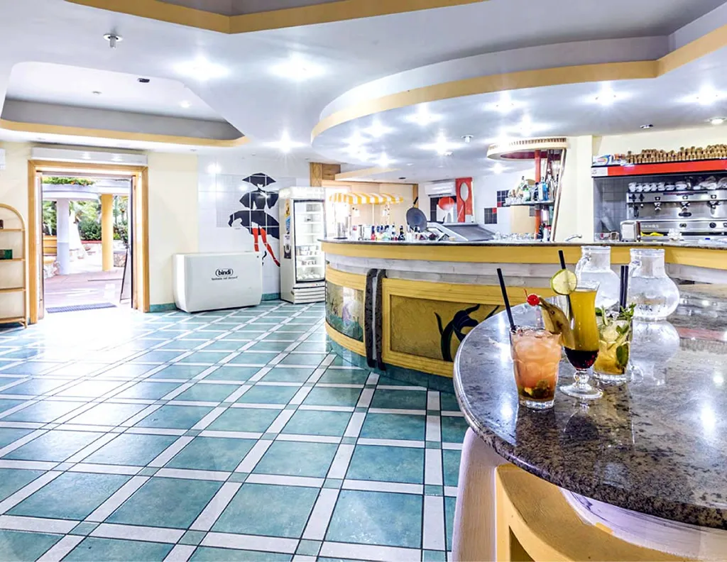 Bar interno con bancone in marmo, cocktail e pavimento a piastrelle turchesi