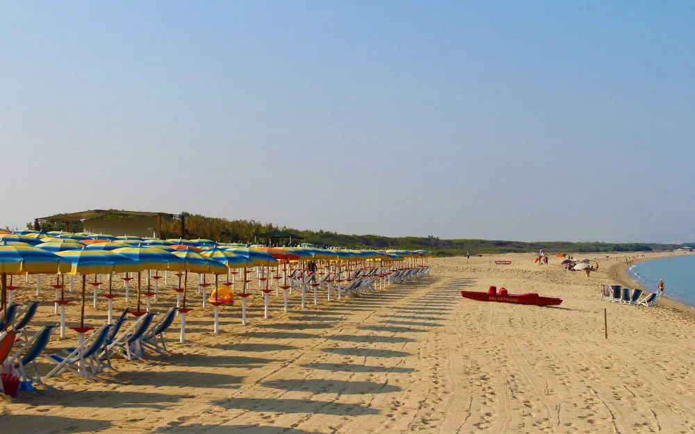 Ampia spiaggia sabbiosa con ombrelloni colorati e lettini lungo la riva