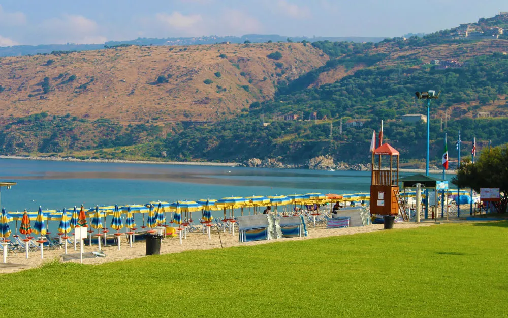 Spiaggia attrezzata con ombrelloni gialli e blu vicino al mare e colline sullo sfondo