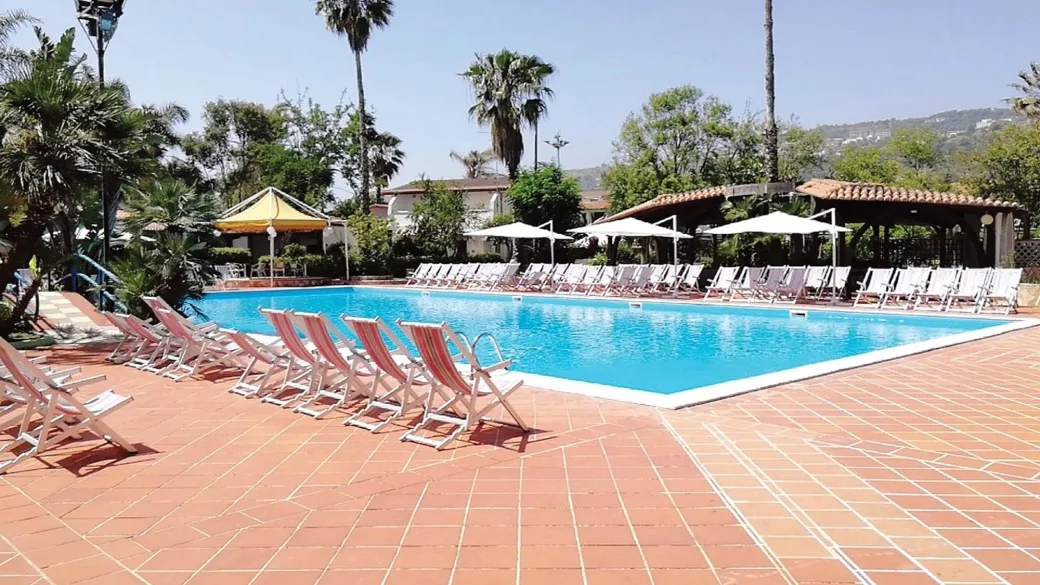 Piscina rettangolare con lettini a righe e ombrelloni bianchi su pavimentazione in cotto
