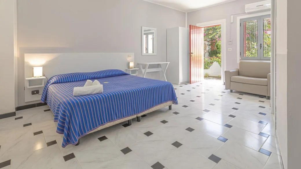 Camera luminosa con letto matrimoniale, copriletto blu a righe e pavimento in marmo