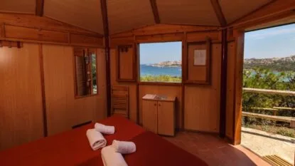 Cameretta di legno con vista sul mare e tessuti arrotolati sul letto.