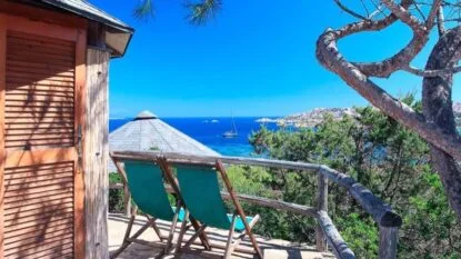 Due sdraio verdi affacciate su un panorama marittimo sereno, con un albero e una casa di legno in un contesto naturale.