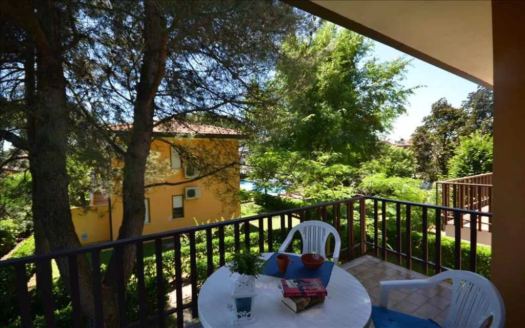 Balcone con tavolo e sedie affacciato sul verde e la piscina del residence