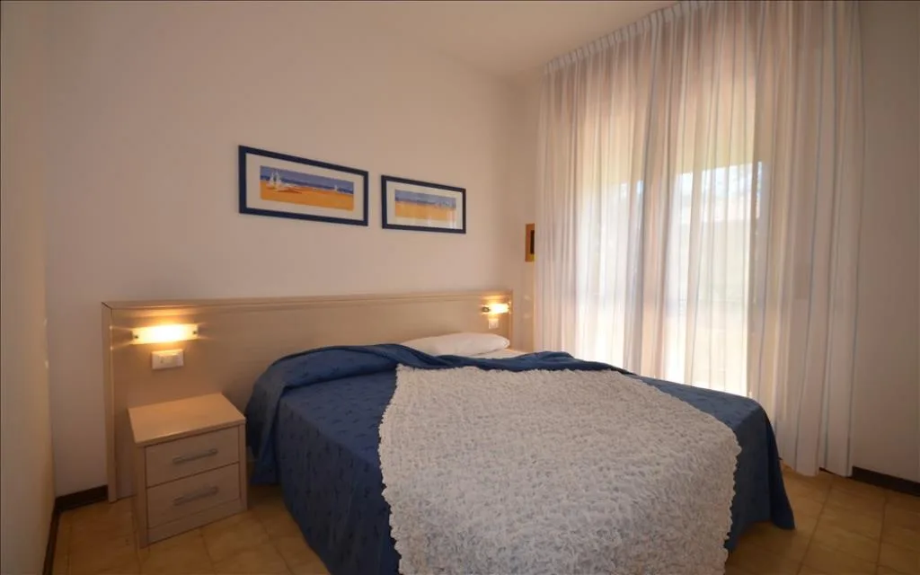 Camera matrimoniale con letto blu, comodino e ampia finestra luminosa