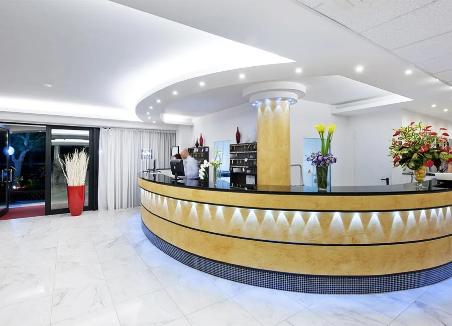 Reception moderna dell'hotel con bancone curvo dorato illuminato e fiori