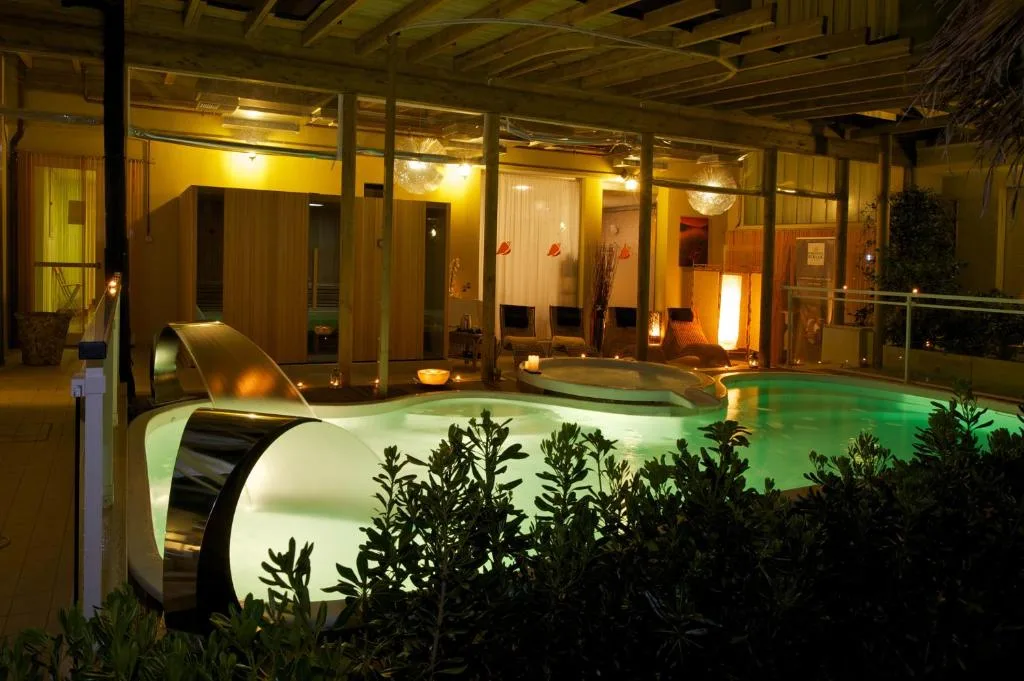 Area spa con piscina interna illuminata, cascata d'acqua e atmosfera rilassante serale