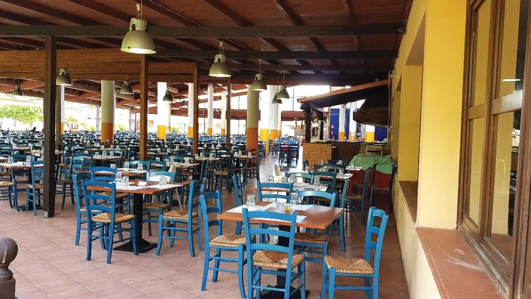 Ampia sala ristorante coperta con tavoli e sedie blu sotto travi in legno