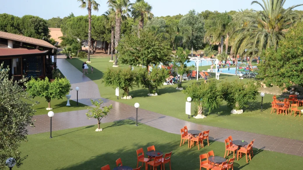Giardino curato con palme, prato verde e tavolini arancioni vicino alla piscina