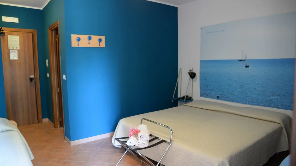 Camera con parete blu e fotografia del mare alle spalle del letto matrimoniale