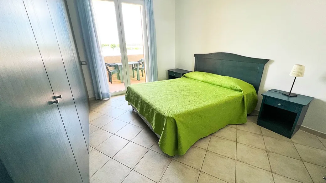 Camera con letto matrimoniale, copriletto verde, armadio e accesso al balcone
