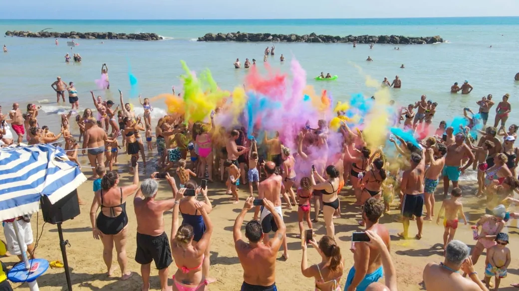 Festa in spiaggia con esplosione di polveri colorate e turisti che si divertono sul bagnasciuga