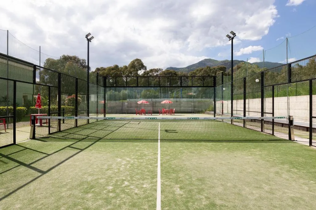 Campo da padel in erba sintetica con recinzione e montagne sullo sfondo