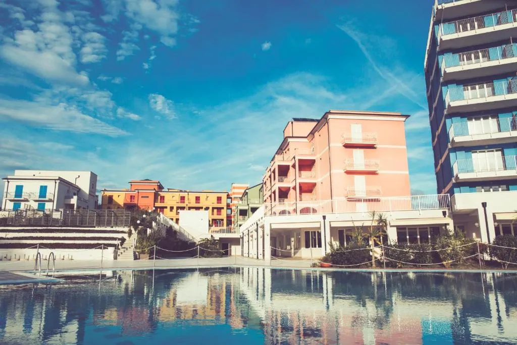 Esterno del resort con edifici colorati e piscina riflettente sotto cielo azzurro