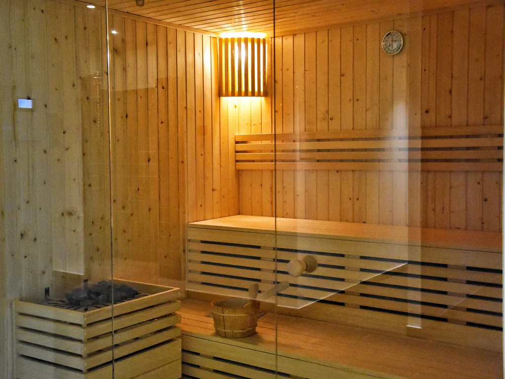 Sauna in legno con parete vetrata e stufa con pietre