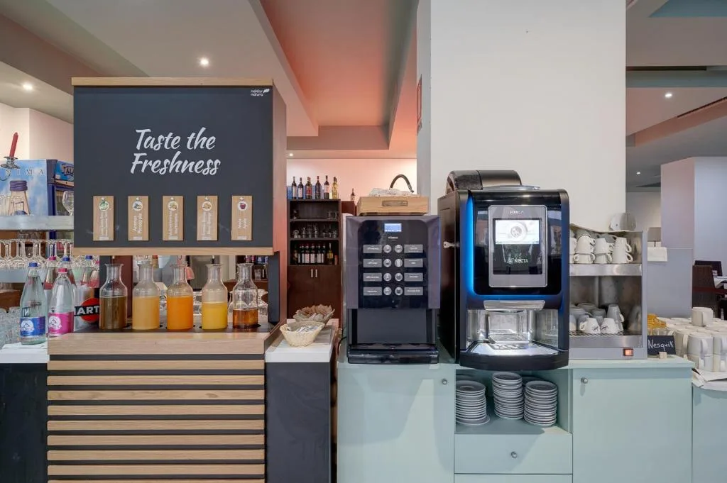 Angolo bevande del buffet con macchine per caffè, succhi e insegna 'Taste the Freshness'
