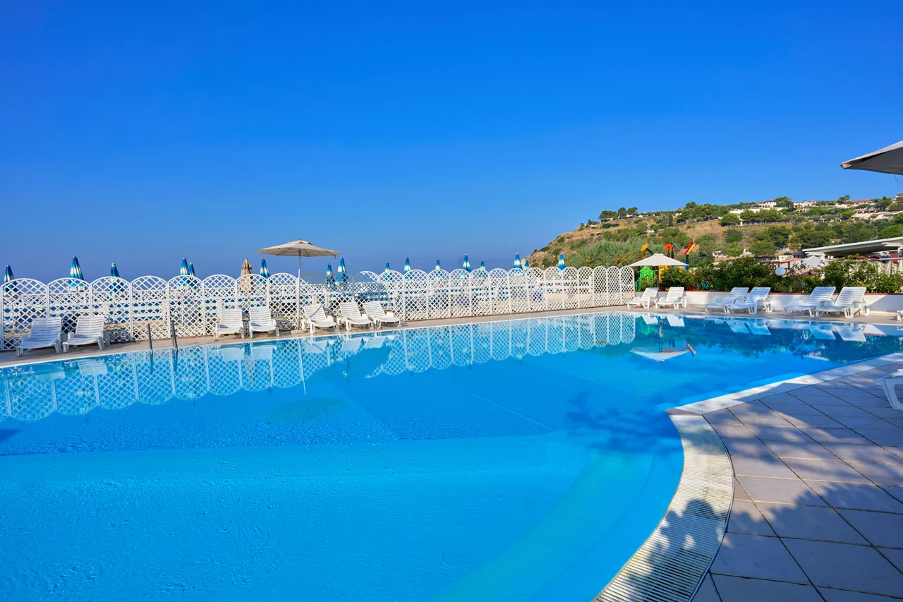 Piscina blu con lettini bianchi e staccionata con vista sulle colline