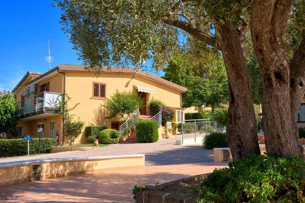 Edificio giallo del villaggio con giardino e ulivo in primo piano