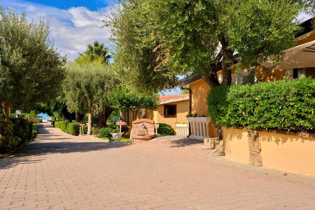 Vialetto del villaggio tra ulivi, siepi e bungalow gialli