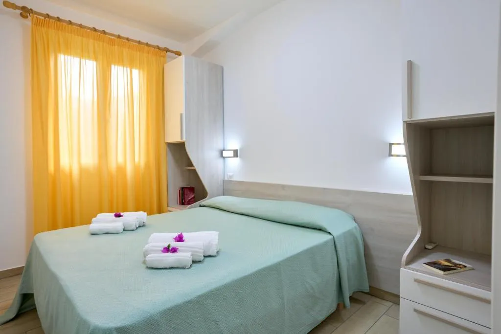 Camera da letto matrimoniale con tende gialle, copriletto verde e asciugamani