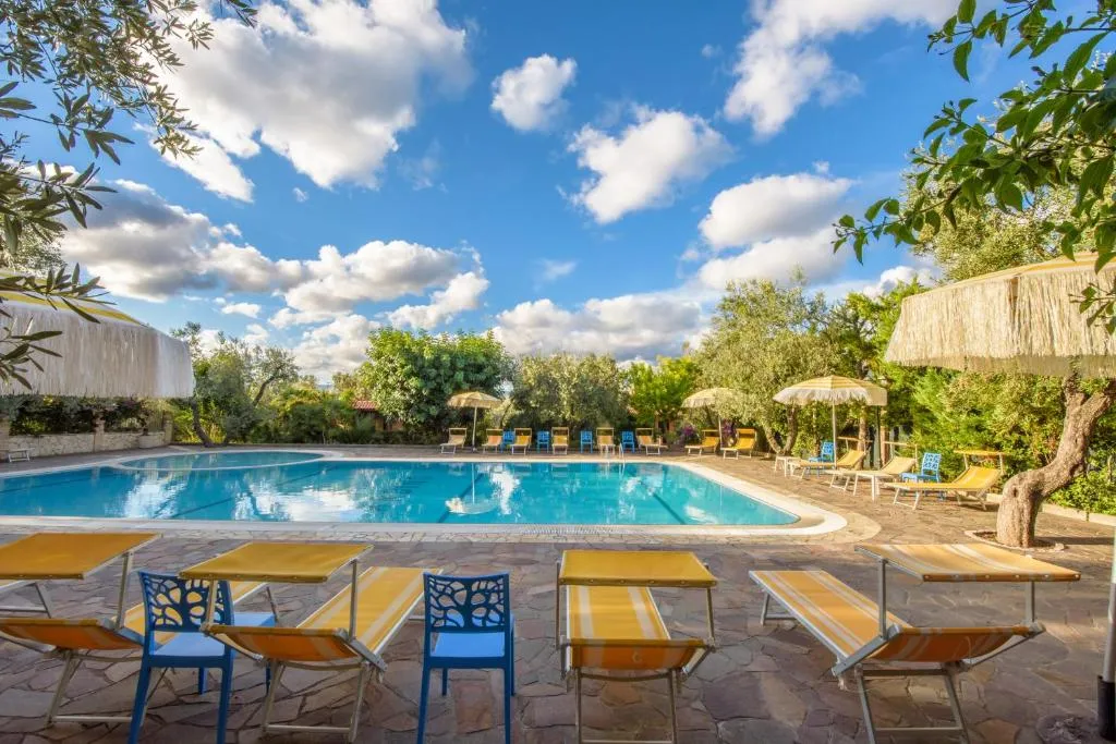 Piscina con lettini gialli e sedie blu su pavimentazione in pietra sotto cielo nuvoloso