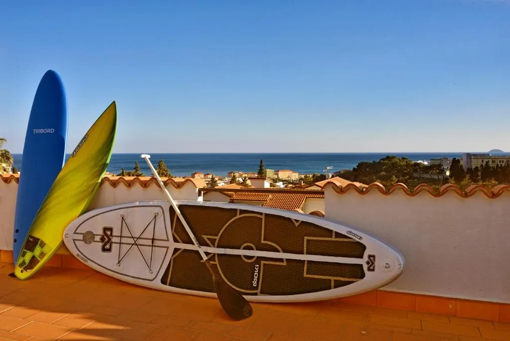Tavole da surf e SUP appoggiate su una terrazza con vista sul mare e sui tetti del paese