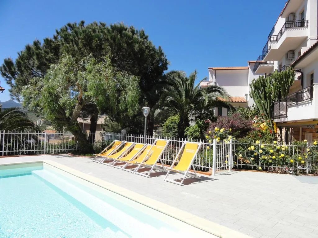 Bordo piscina con lettini gialli, vegetazione fiorita e edificio residenziale bianco