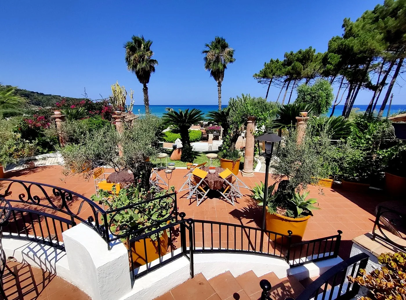 Ampia terrazza panoramica con palme, pini e vista sul mare cristallino