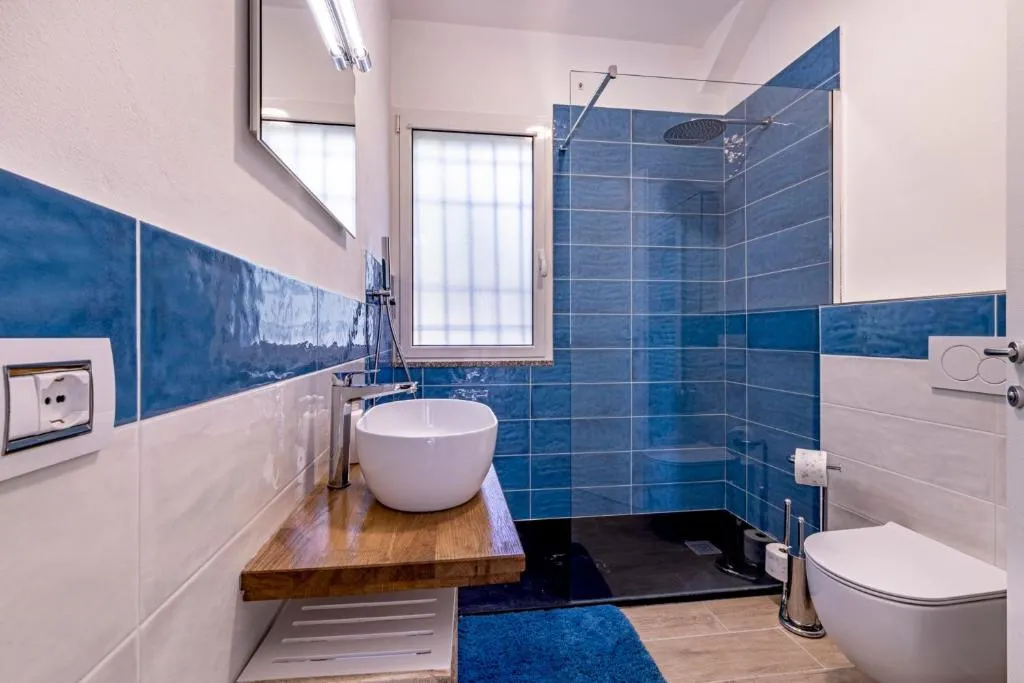 Bagno moderno con piastrelle blu, lavabo bianco su mensola in legno e doccia walk-in