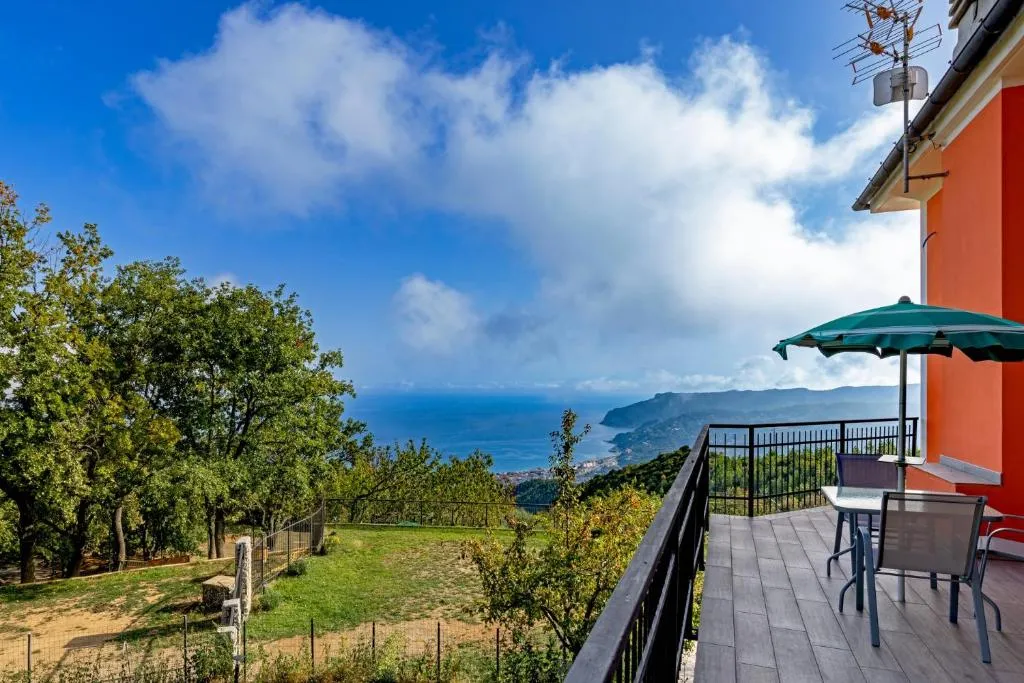 Balcone con tavolo, sedie e ombrellone verde con vista panoramica sul mare e la costa