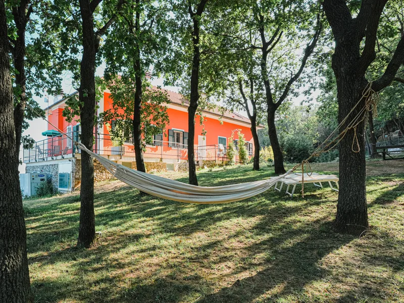 Amaca tra gli alberi nel giardino con la villa arancione sullo sfondo