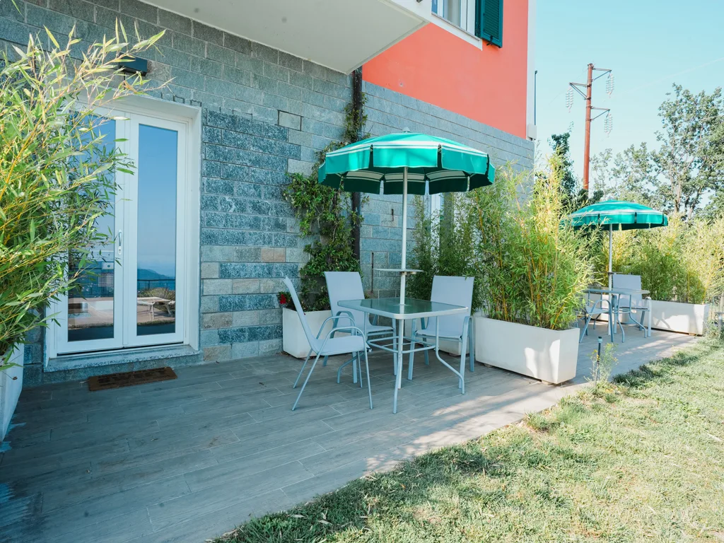 Terrazza esterna con tavolo, sedie e ombrelloni verdi accanto alla parete in pietra