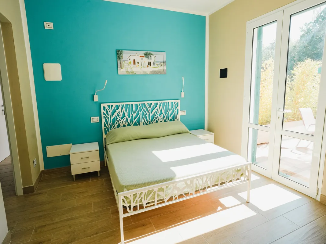 Camera da letto luminosa con parete turchese, letto matrimoniale e porta finestra sul terrazzo